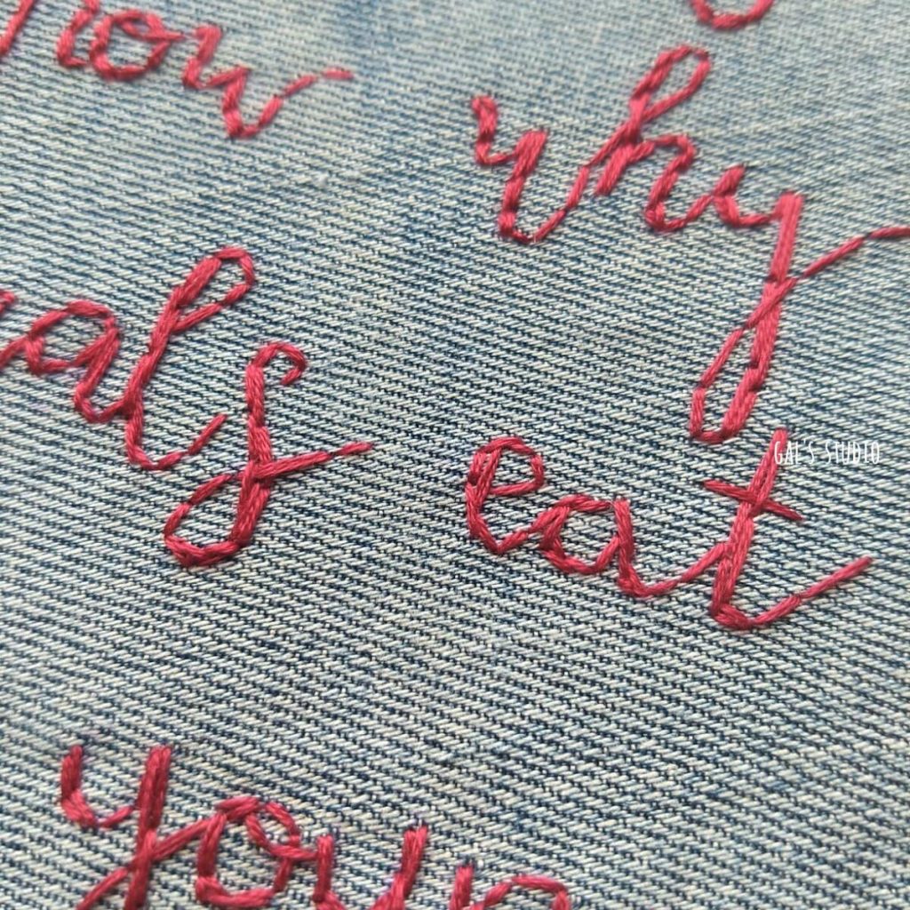 תקריב על רקמת כתב מחובר באנגלית, חוט אדום על ג'ינס